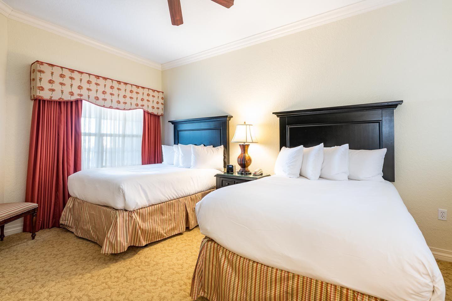 Une chambre d’hôtel avec deux lits, une table de chevet avec une lampe et une fenêtre avec des rideaux rouges.