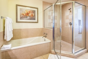 Un baño con bañera, ducha con mampara de cristal y un cuadro con flores en la pared.