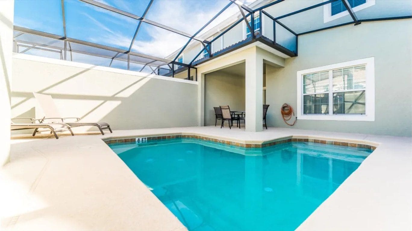 An indoor swimming pool with a clear glass ceiling, a table and chairs, and a window with blinds.