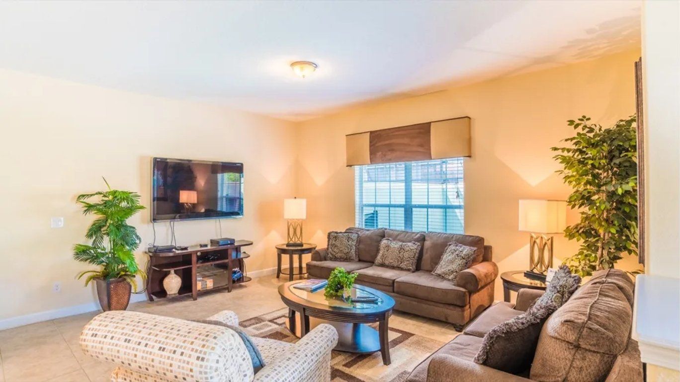 A living room with a sofa, armchairs, a coffee table, a TV, and two lamps.