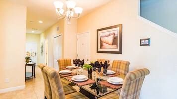 A dining area with a glass-top table, plaid chairs, and a chandelier.