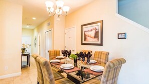 A dining area with a glass-top table, plaid chairs, and a chandelier. - Paradise Palms - 6166 (Kissimmee)