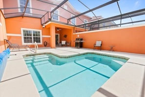 An indoor swimming pool with a glass ceiling, surrounded by orange walls and a patio area with chairs and a barbecue. - Paradise Palms - 6180 (Kissimmee)