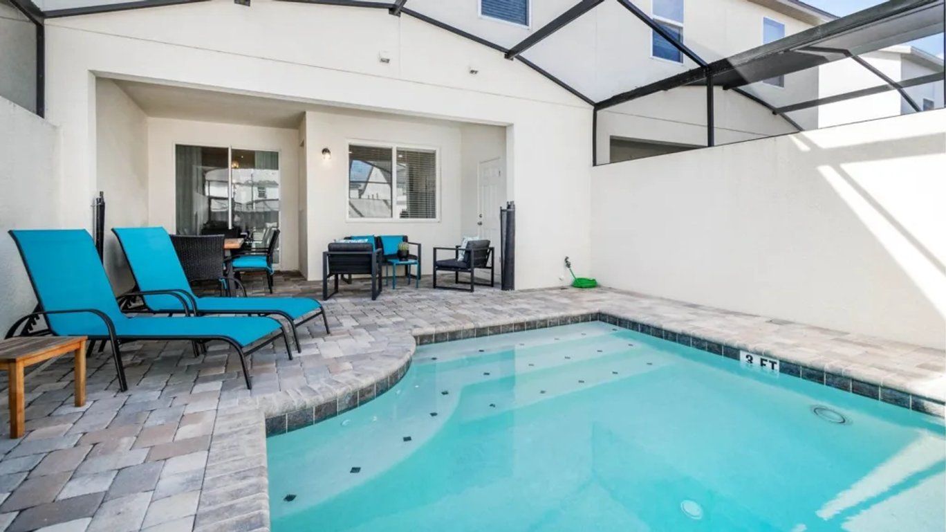 A swimming pool with lounge chairs and a table, surrounded by a covered patio area.