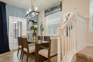 A dining area with a glass table and chairs, a chandelier, and a staircase with white railings. - Windsor Island - 6336 (Davenport)