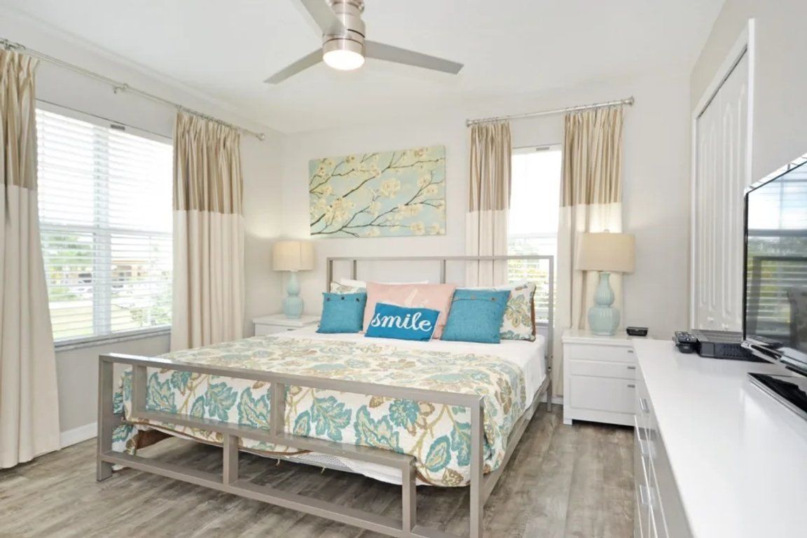 A bedroom with a bed, bedside tables, a ceiling fan, and a window with curtains.