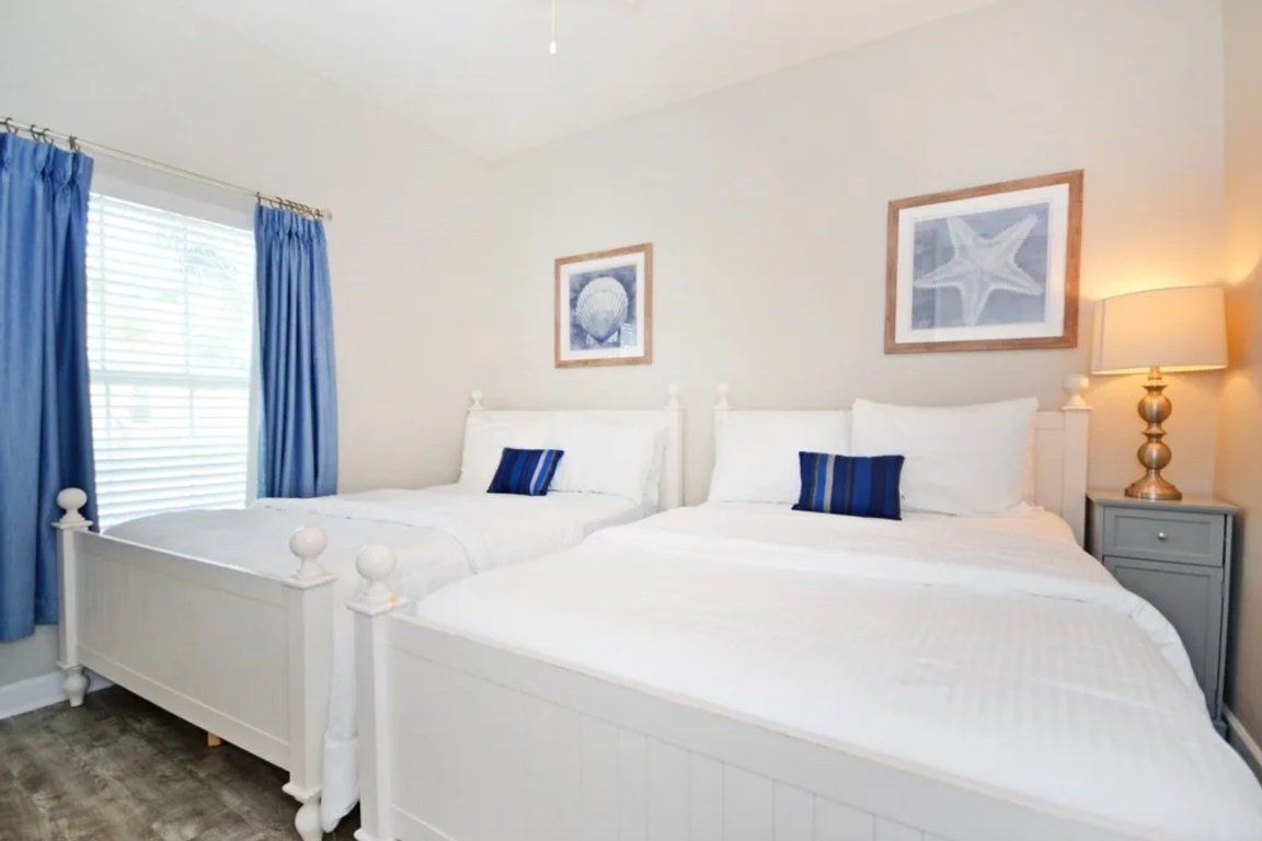 A bedroom with two white beds, a nightstand, a lamp, and a framed picture on the wall.