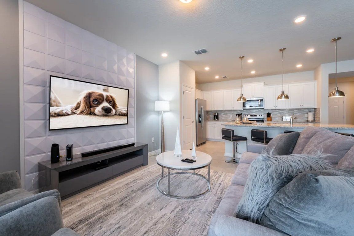 A modern living room with a flat-screen TV, a round coffee table, and a grey sofa.