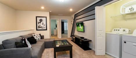 A living room with a gray sofa, a coffee table, a TV, and a laundry area with a washing machine.