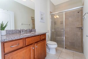 Ein Badezimmer mit Granitplatte, Holzschränken, einer weißen Toilette und einer Duschkabine.