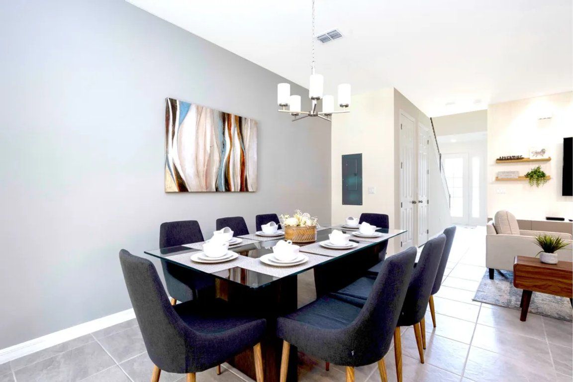 A modern dining area with a rectangular table set for six, surrounded by dark upholstered chairs with wooden legs.