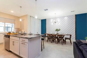 A modern kitchen with a central island, dining area with chairs, and a blue accent wall. - Solara Resort - 6766 (Kissimmee)