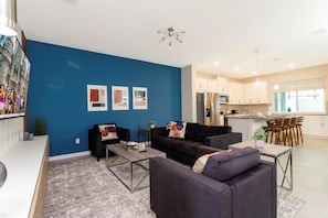 A modern living room with a blue accent wall, a sofa, a coffee table, and a kitchen in the background. - Solara Resort - 6766 (Kissimmee)