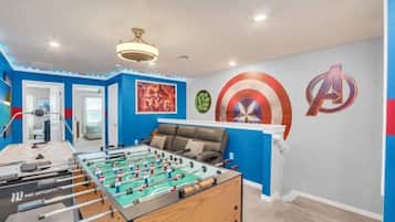 Una habitación con mesa de futbolín, una cama y una pared decorada con motivos de superhéroes.