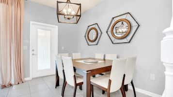 Un comedor con una mesa de madera y sillas blancas, una araña y dos espejos hexagonales en la pared.