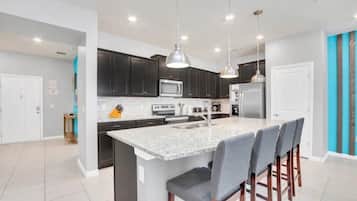 Una cocina moderna con armarios oscuros, una isla central con taburetes altos e iluminación colgante.