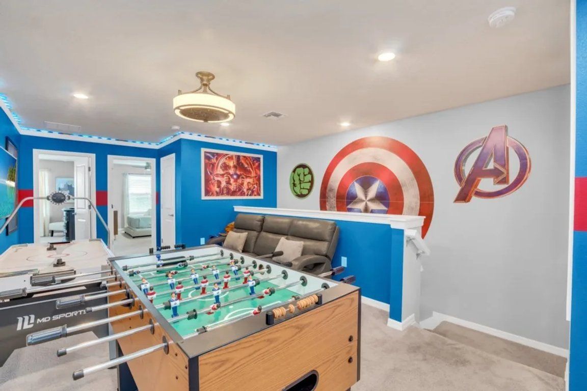 Una habitación con mesa de futbolín, una cama y una pared decorada con motivos de superhéroes.