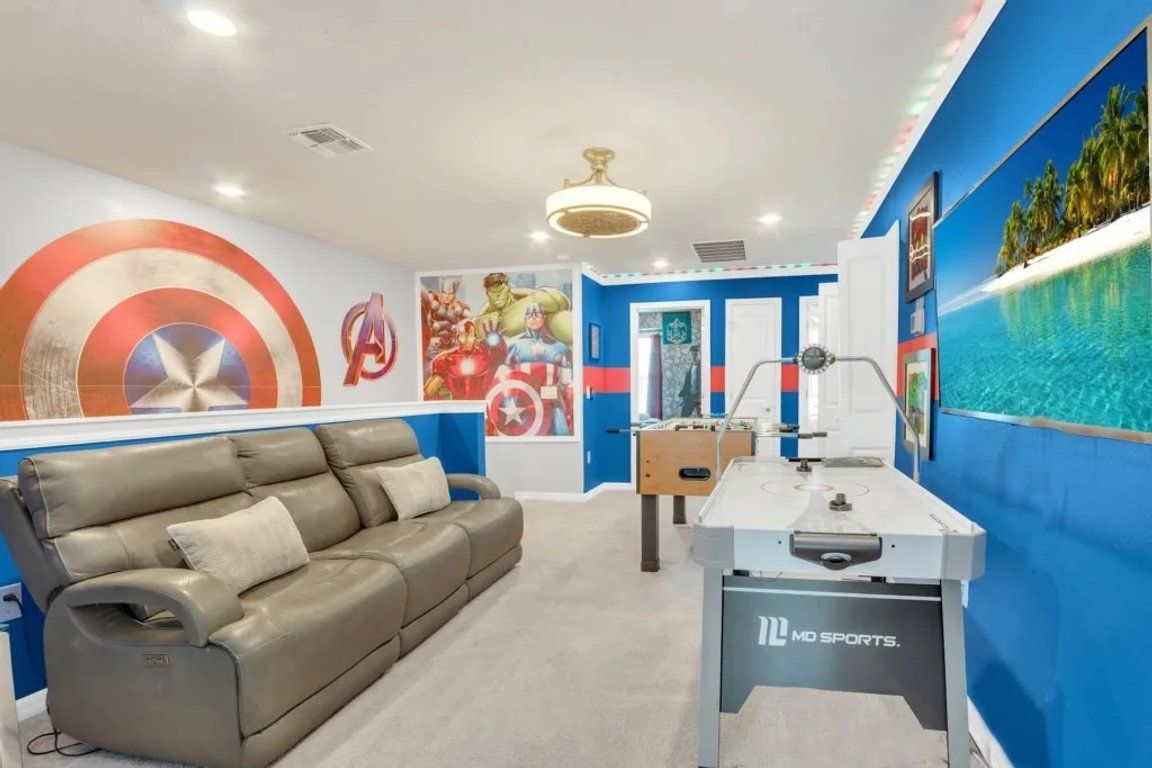 Una habitación con sofá de cuero, mesa de fútbol y pared decorada con ilustraciones de superhéroes.