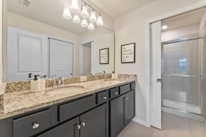 A bathroom with a large mirror, a granite countertop, dark cabinets, and a glass shower enclosure. - Windsor Island - 7358 (Davenport)