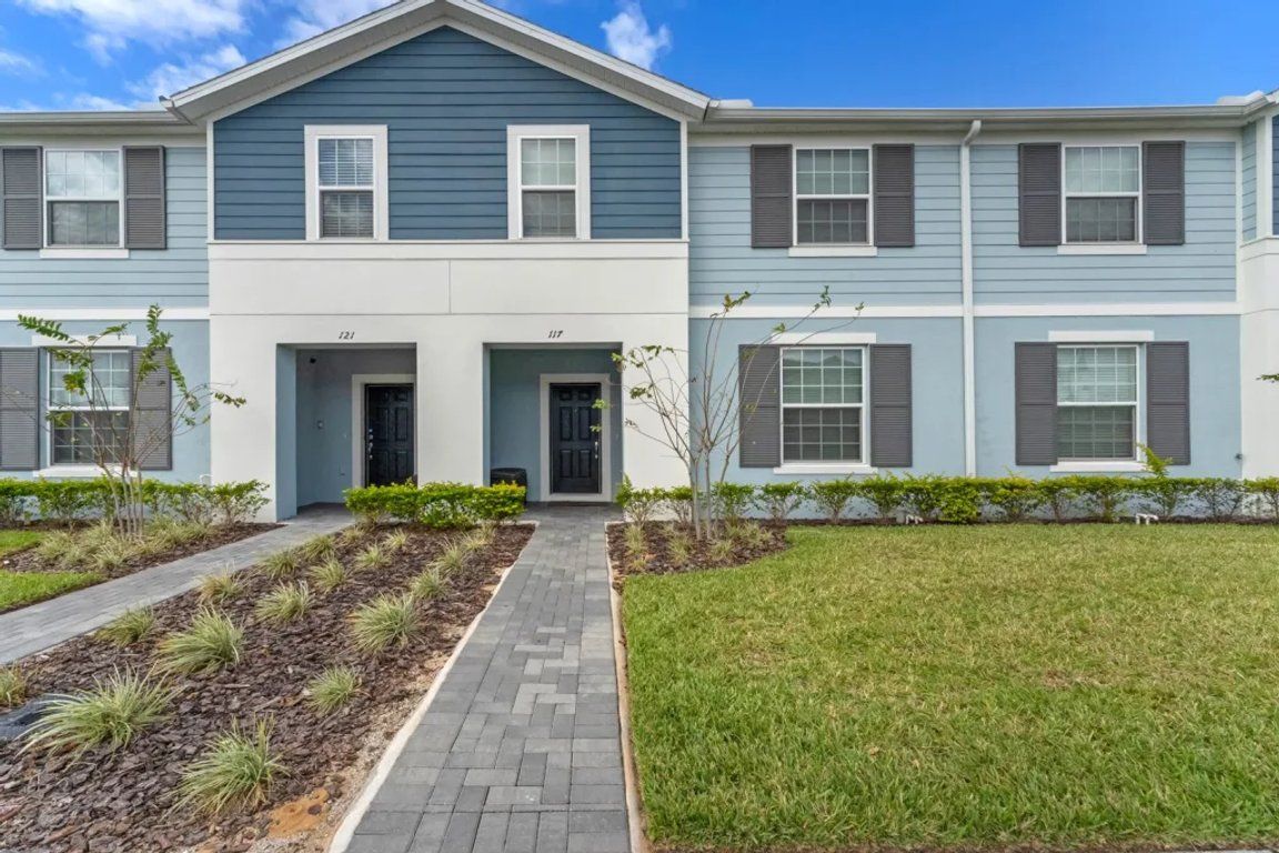 A two-story residential building with a central entrance, a paved walkway, and a well-maintained lawn.