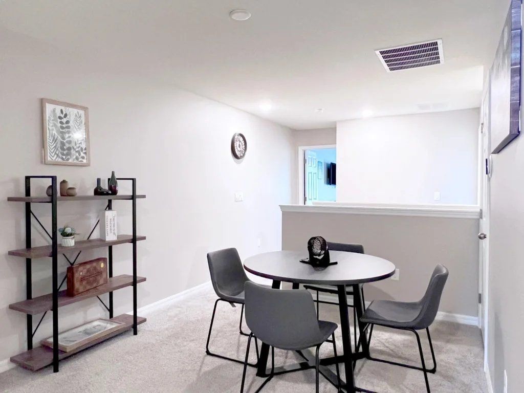 A room with a round table and four chairs, a bookshelf, and a window with a view.