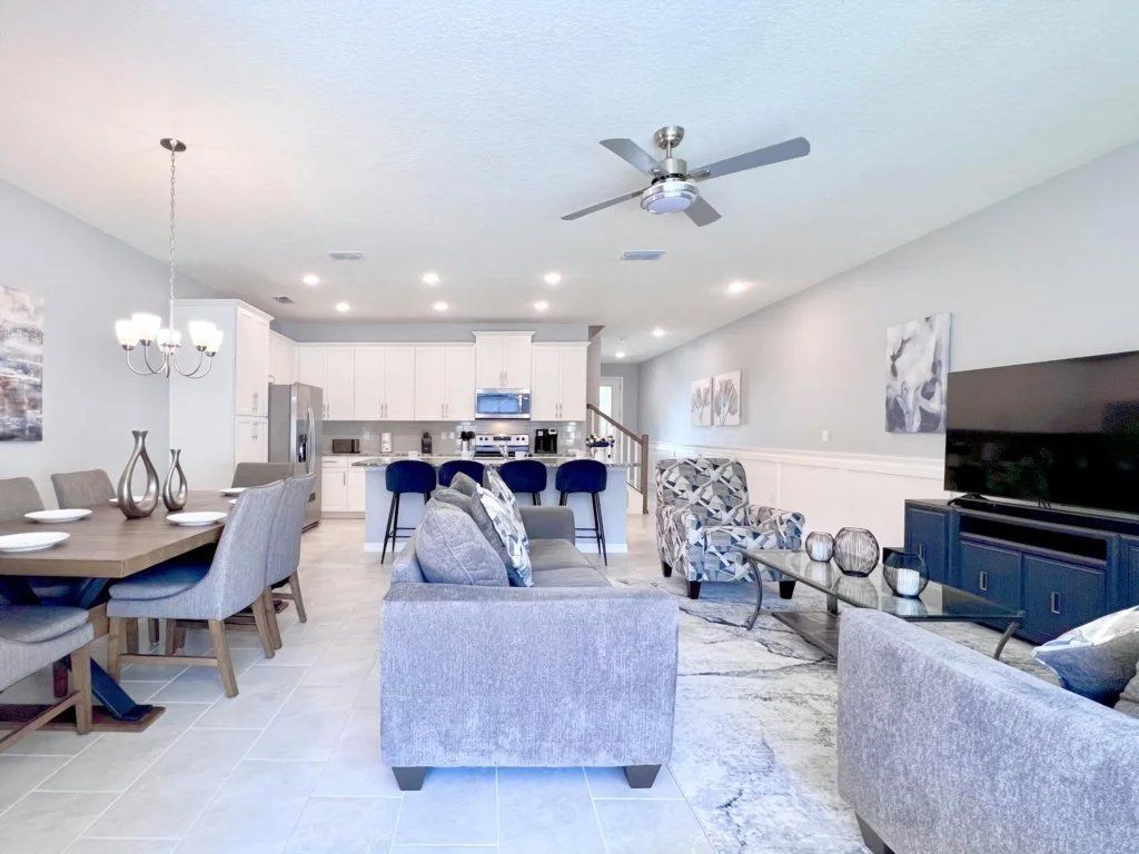 A modern living room with a dining area, a kitchen in the background, and a ceiling fan.