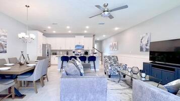 A modern living room with a dining area, a kitchen in the background, and a ceiling fan.
