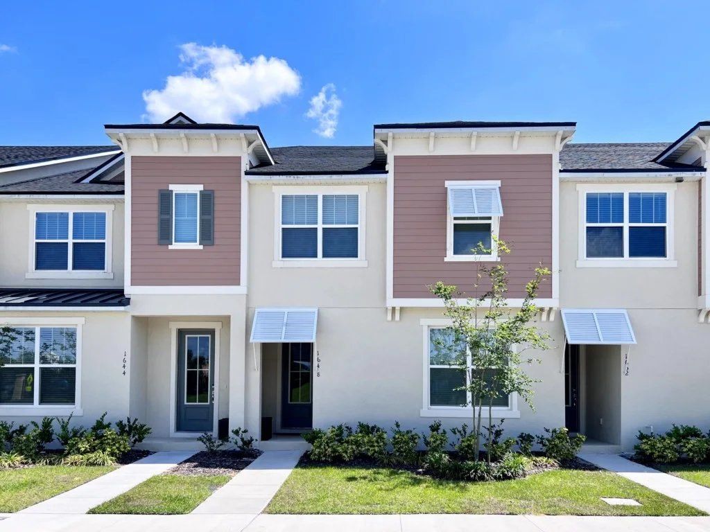A row of townhouses with a front entrance, a small tree, and a clear sky.