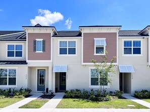 A row of townhouses with a front entrance, a small tree, and a clear sky. - Solara Resort - 7390 (Kissimmee)