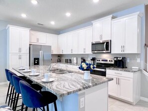 A modern kitchen with white cabinets, a granite countertop, and a stainless steel refrigerator. - Solara Resort - 7390 (Kissimmee)