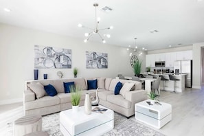 A modern living room with a sectional sofa, a glass coffee table, and a dining area with a kitchen in the background. - Reunion - 7697 (Kissimmee)