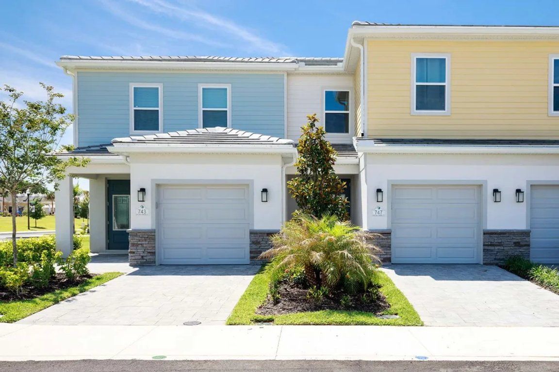 A two-story residential building with a garage, a well-maintained lawn, and a clear sky.