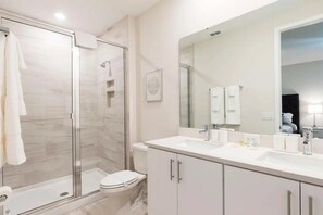A modern bathroom with a glass-enclosed shower, a white toilet, and a vanity with a large mirror. - Reunion - 7697 (Kissimmee)