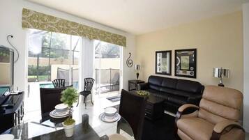 A modern living room with a black leather sofa, a dining table with chairs, and a kitchen area with a black countertop.