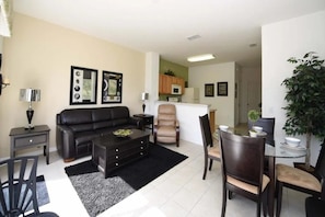 Una sala de estar con un sofá negro, una mesa de centro y un comedor con sillas y una mesa pequeña.