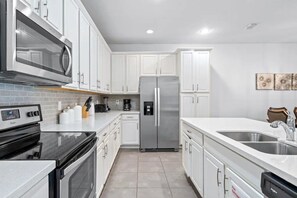A modern kitchen with white cabinets, stainless steel appliances, a microwave, oven, and a refrigerator. - Solara Resort - 7868 (Kissimmee)