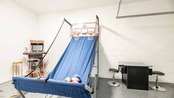 Une pièce avec un toboggan bleu, un panier de basket et une petite table avec des tabourets.