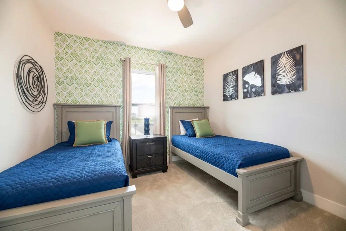 Une chambre avec deux lits, un ventilateur de plafond et une fenêtre avec des rideaux.