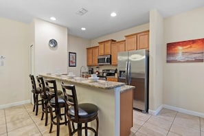 A kitchen with a central island, wooden cabinets, stainless steel appliances, and a clock on the wall. - Paradise Palms - 11473 (Kissimmee)