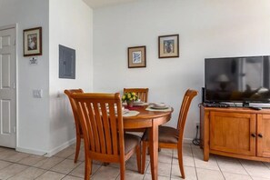 A dining area with a round table, wooden chairs, a television on a wooden cabinet, and framed pictures on the wall. - Windsor Palms - 11478 (Kissimmee)