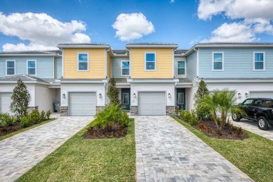 A row of townhouses with individual garages, a paved driveway, and small landscaped areas.