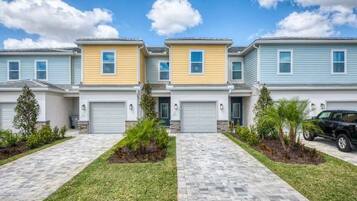 A row of townhouses with individual garages, a paved driveway, and small landscaped areas.