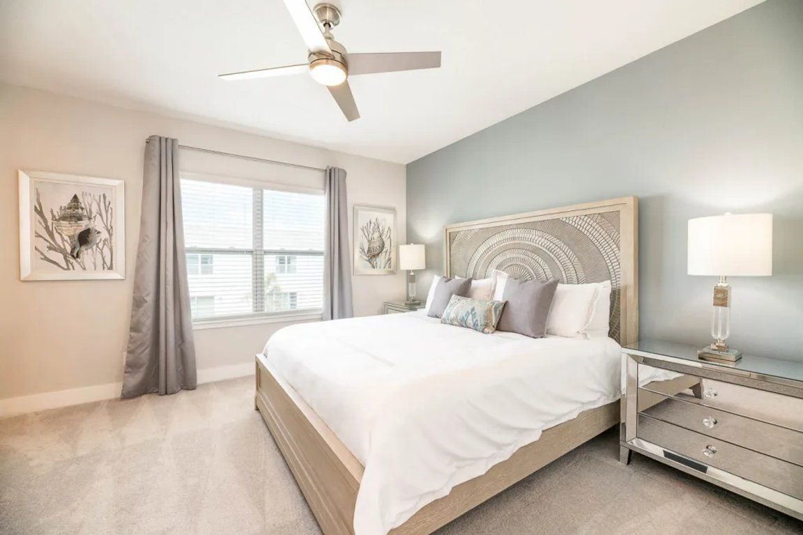 A bedroom with a bed, nightstands, a ceiling fan, and artwork on the walls.