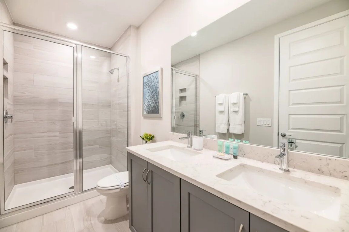 A modern bathroom with a glass shower enclosure, a toilet, a vanity with a sink, and a large mirror.