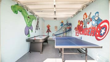 Una habitación con mesa de ping pong, mesa de billar y un mural de personajes de Marvel.