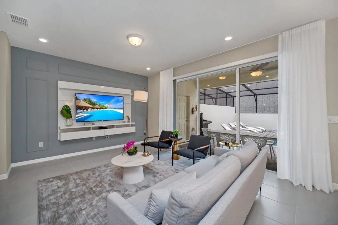 A modern living room with a flat-screen TV, a sofa, a coffee table, and a dining area with chairs.