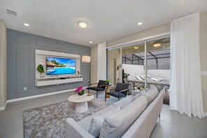 A modern living room with a flat-screen TV, a sofa, a coffee table, and a dining area with chairs. - Windsor Island - 26298 (Davenport)