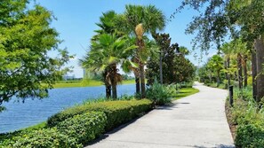 A paved pathway alongside a body of water, flanked by lush greenery and palm trees. - Vista Cay - 28926 (Orlando)