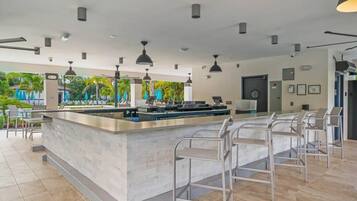 Un área de bar moderna con una barra larga, taburetes metálicos y lámparas colgantes.