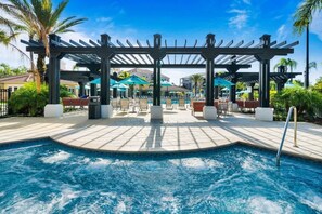 A pool area with a hot tub, lounge chairs, and umbrellas. - Vista Cay - 28975 (Orlando)